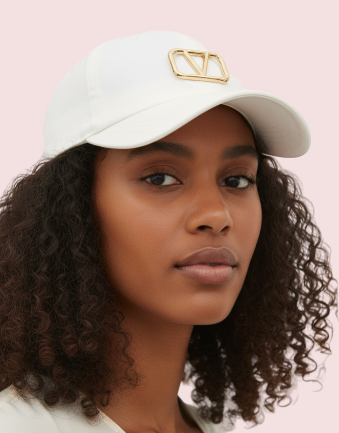 Woman wearing a white cap with a gold logo on a plain background